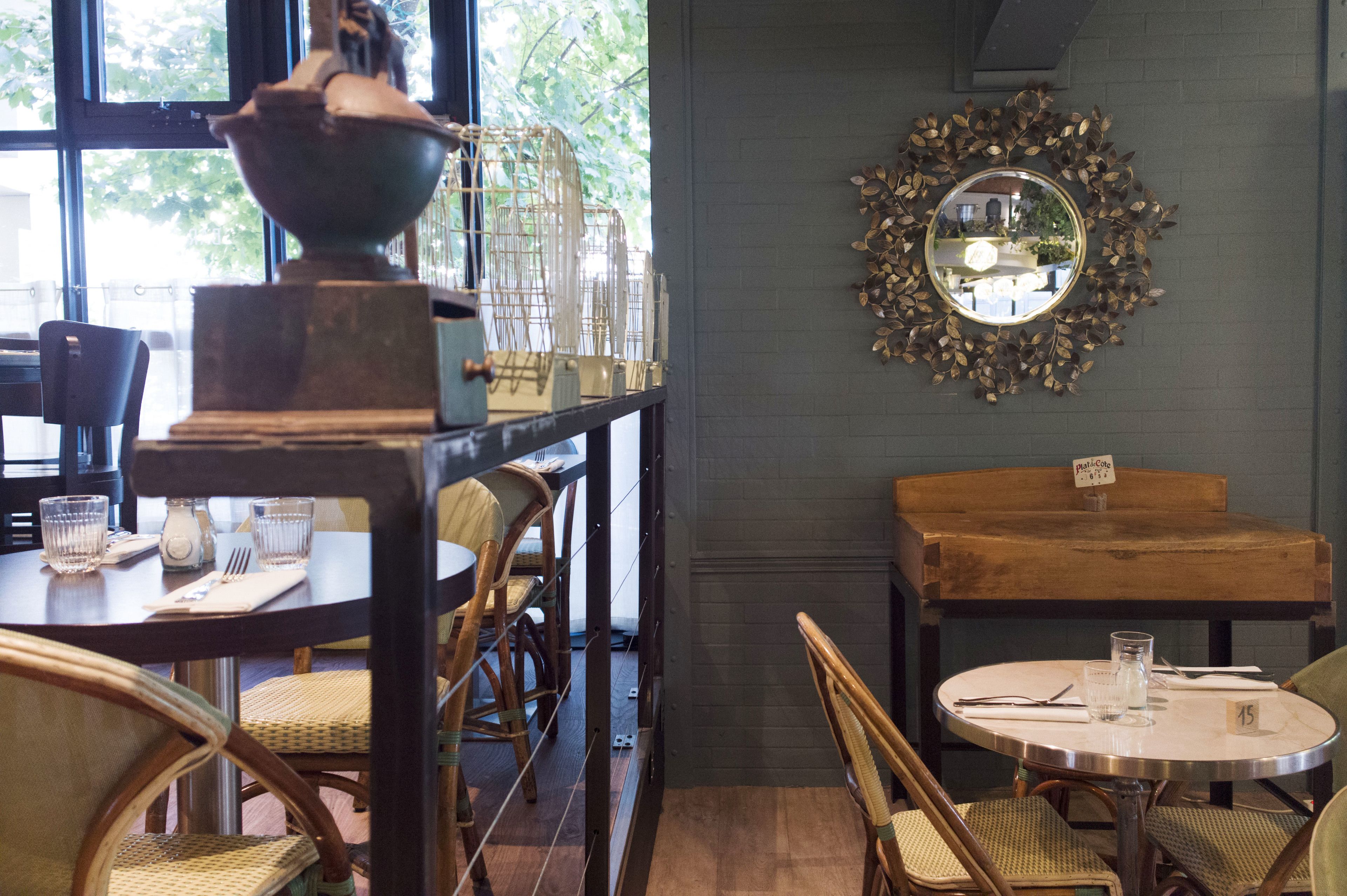 A dining area with wooden tables and chairs, a decorative birdcage, and a mirror on the wall.