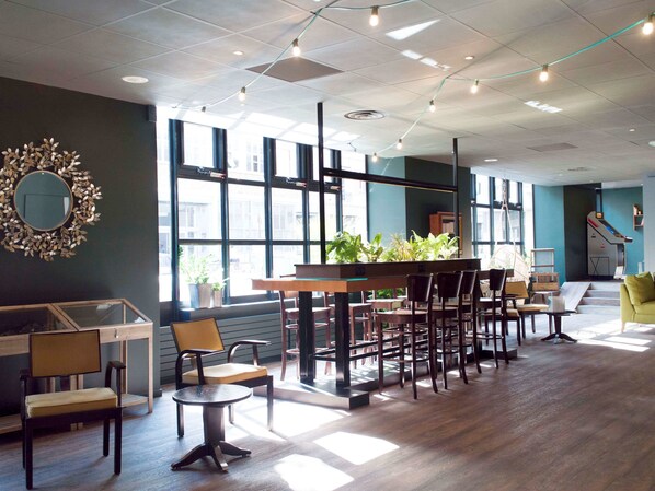 A modern interior with a long table and chairs, large windows, and a staircase. - Hotel ibis Paris Bastille Opera 11ème (Paris)