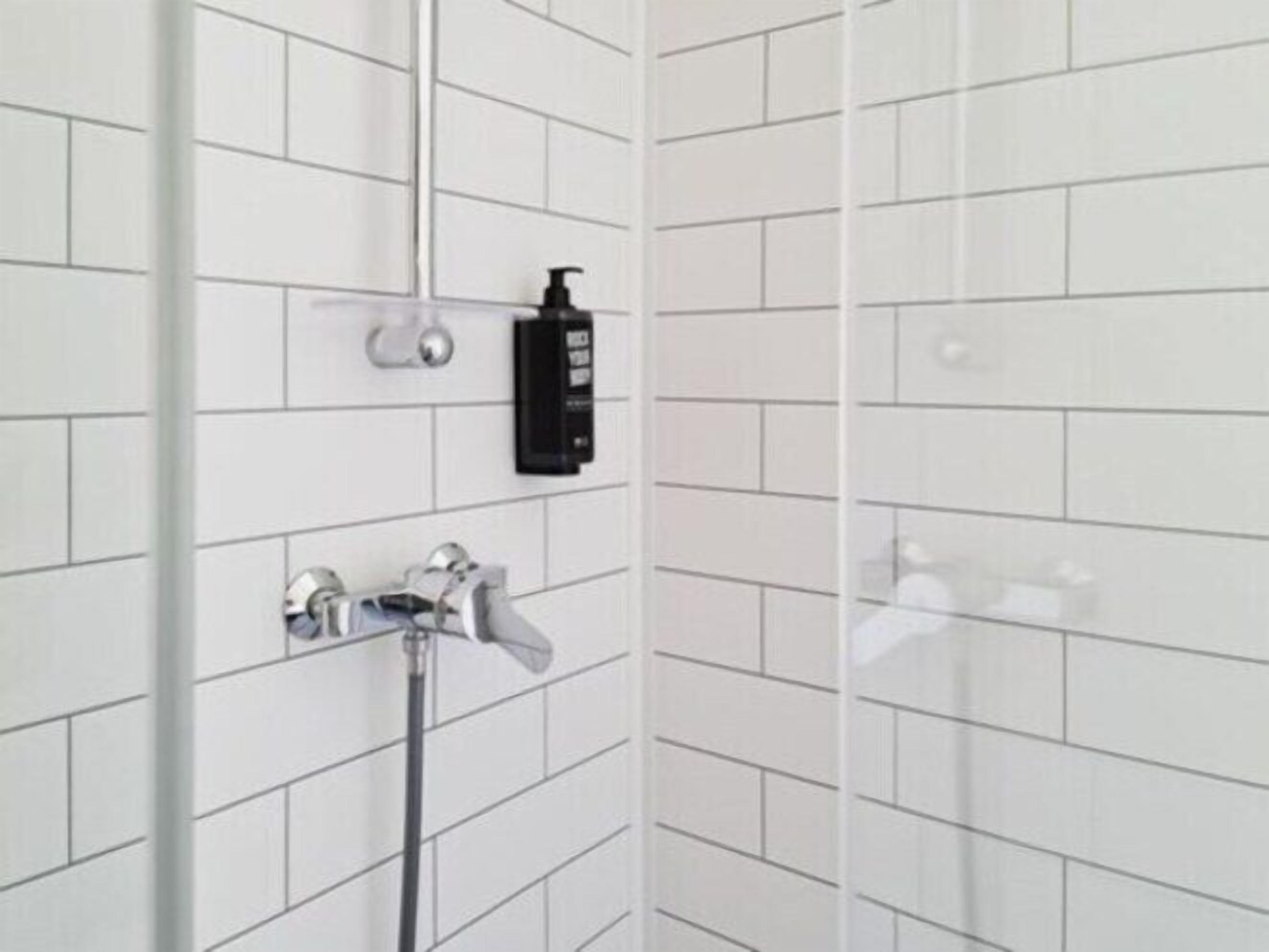 A bathroom with white tiled walls, a shower, a faucet, and a soap dispenser.