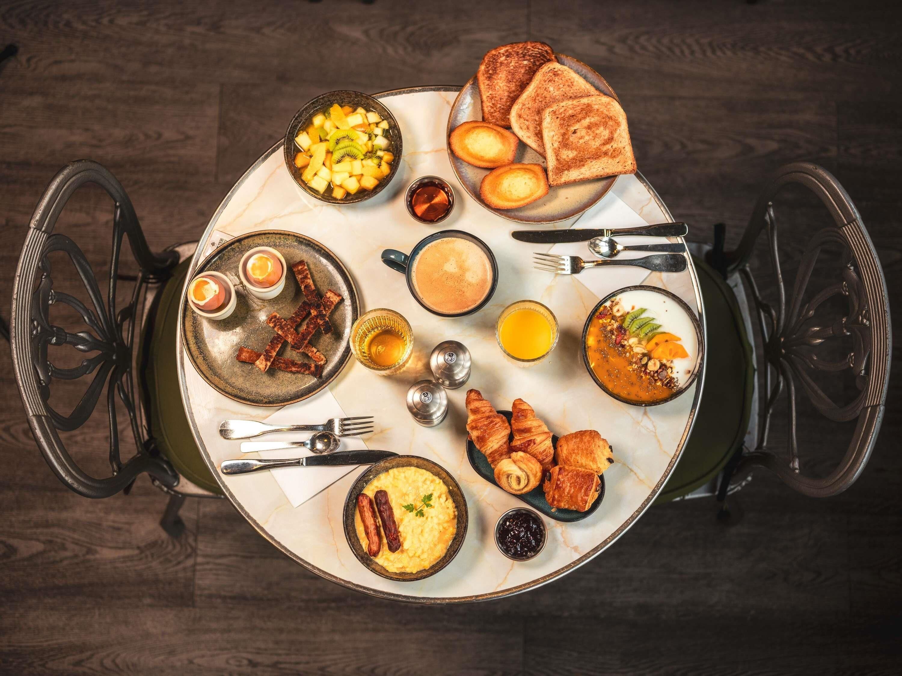 Une table dressée pour le petit-déjeuner avec des toasts, des œufs, des saucisses et un panier de fruits.