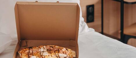 Pizza numa caixa de cartão sobre uma cama com um travesseiro e lençol brancos.
