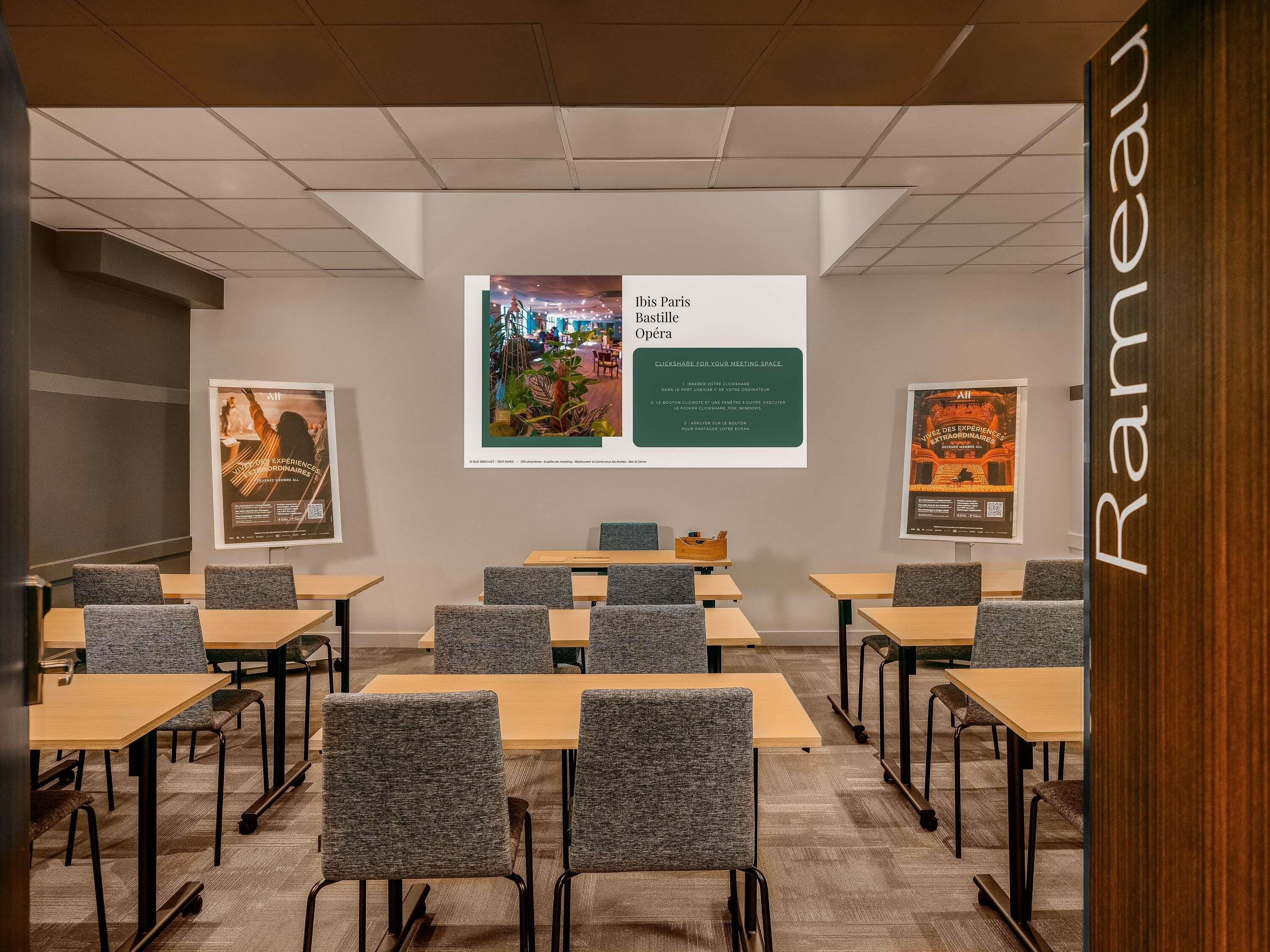 A conference room with tables and chairs, a projector screen, and posters on the walls.