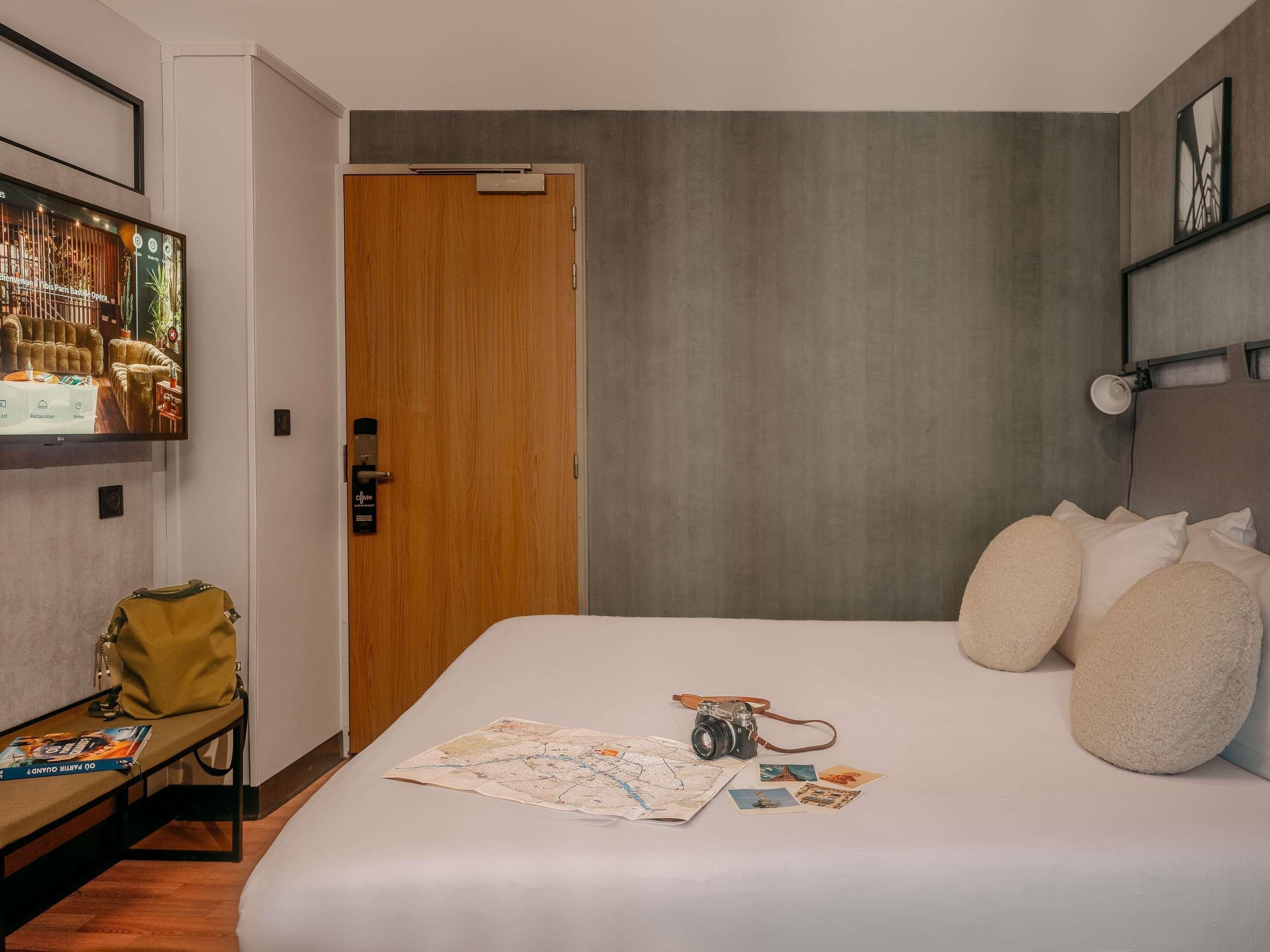 Una habitación de hotel con una cama, un mapa, una cámara y un banco con un bolso.