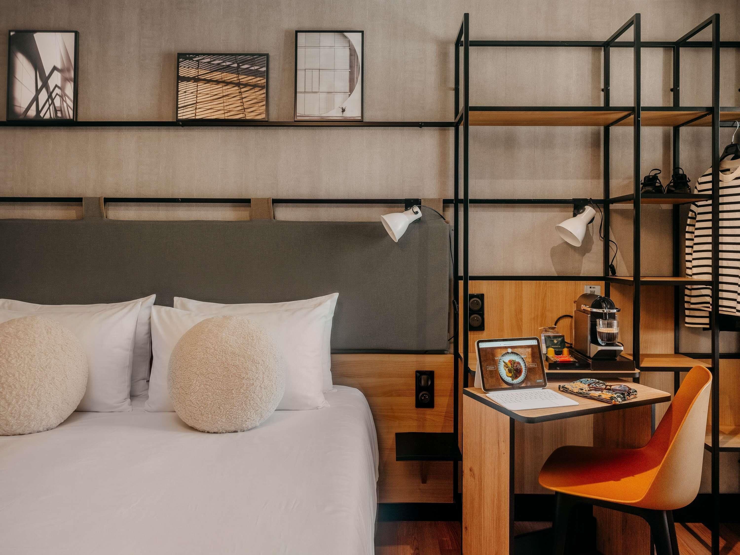 Habitació d'hotel amb un llit, almoines, un escriptori amb un ordinador portàtil, una cafetera i una cadira.