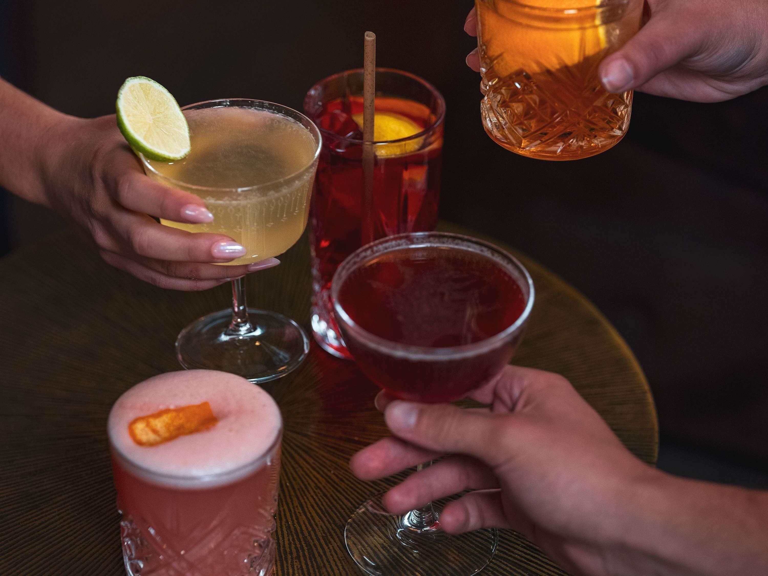 A round table with four glasses of different beverages, a lime wedge, and a straw.