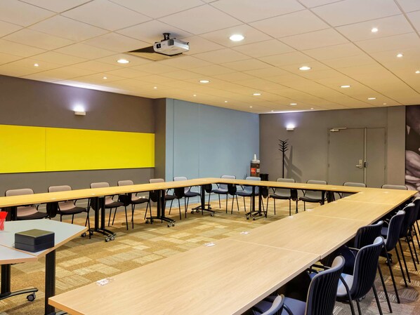 Une salle de conférence équipée d’une longue table, de chaises, d’un projecteur et d’un grand écran.