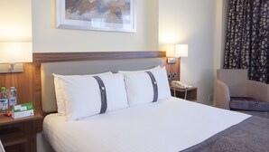 A hotel room with a large bed, two bedside lamps, a telephone, a chair, and a framed artwork on the wall. - Holiday Inn Ipswich by IHG (Ipswich)