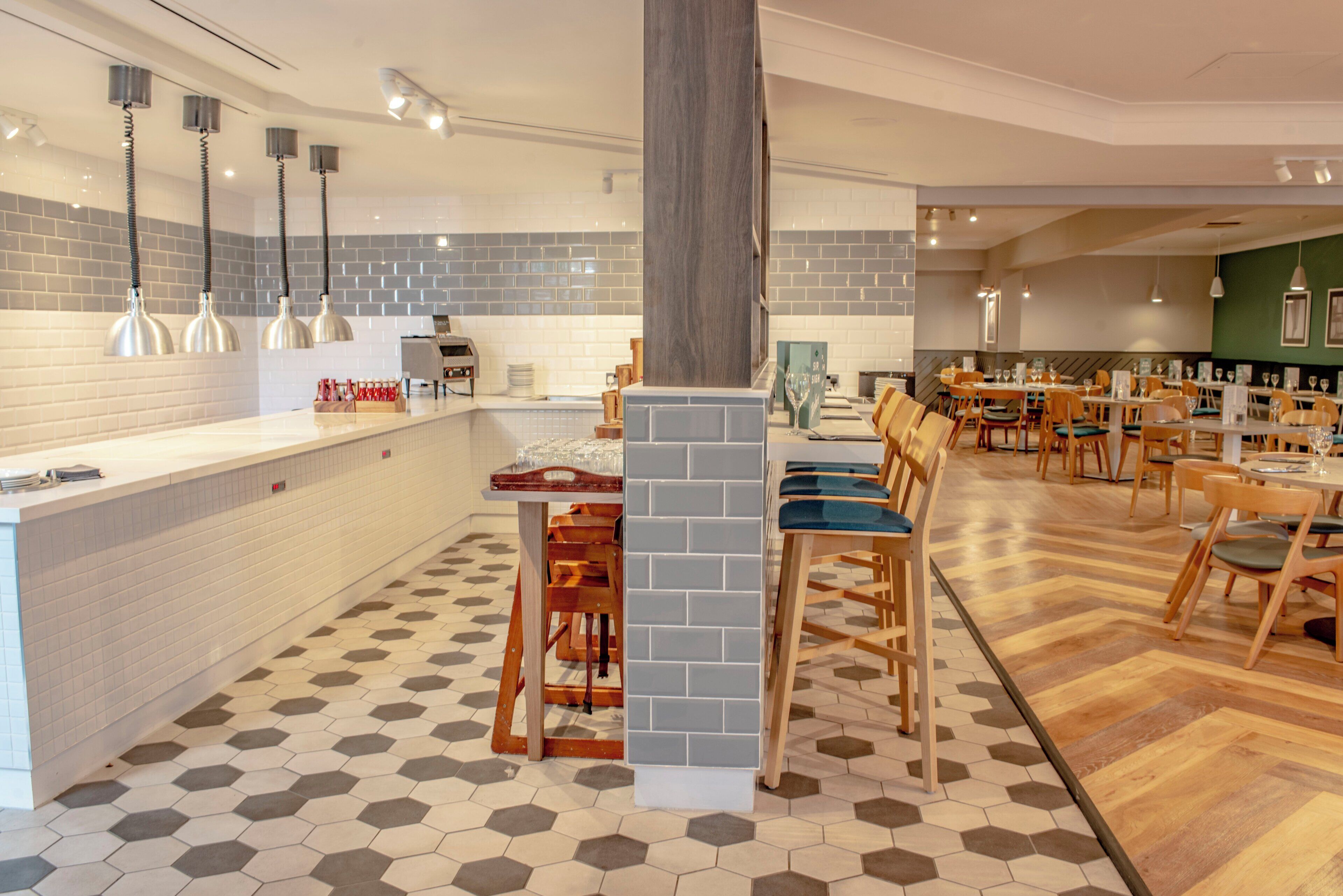 A restaurant with a long counter, multiple tables, and hexagonal patterned flooring.