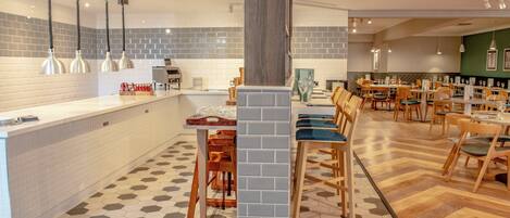 Un restaurante con una barra larga, varias mesas y un suelo con estampado hexagonal.