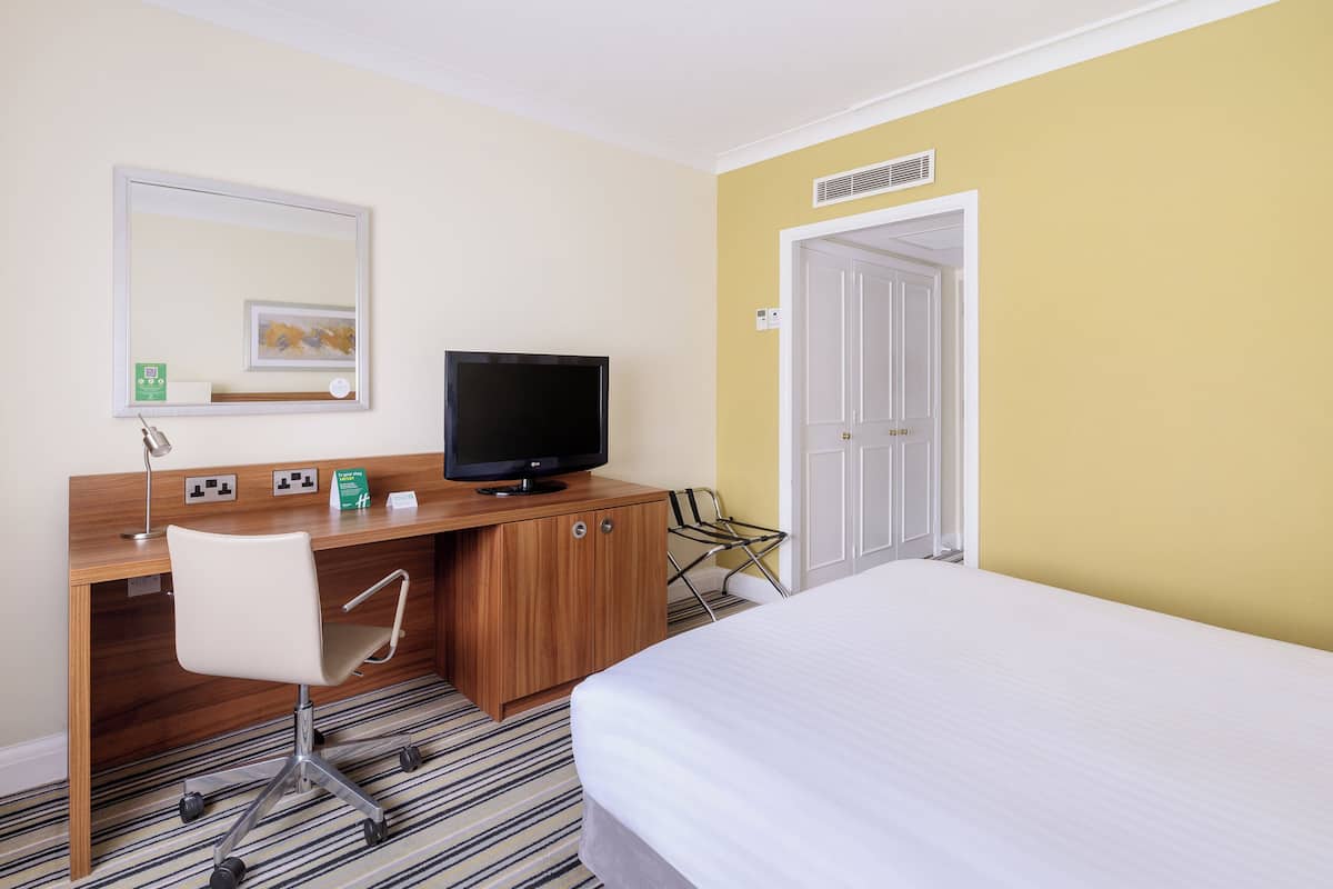 A hotel room with a bed, a desk with a chair, a television, and a door.