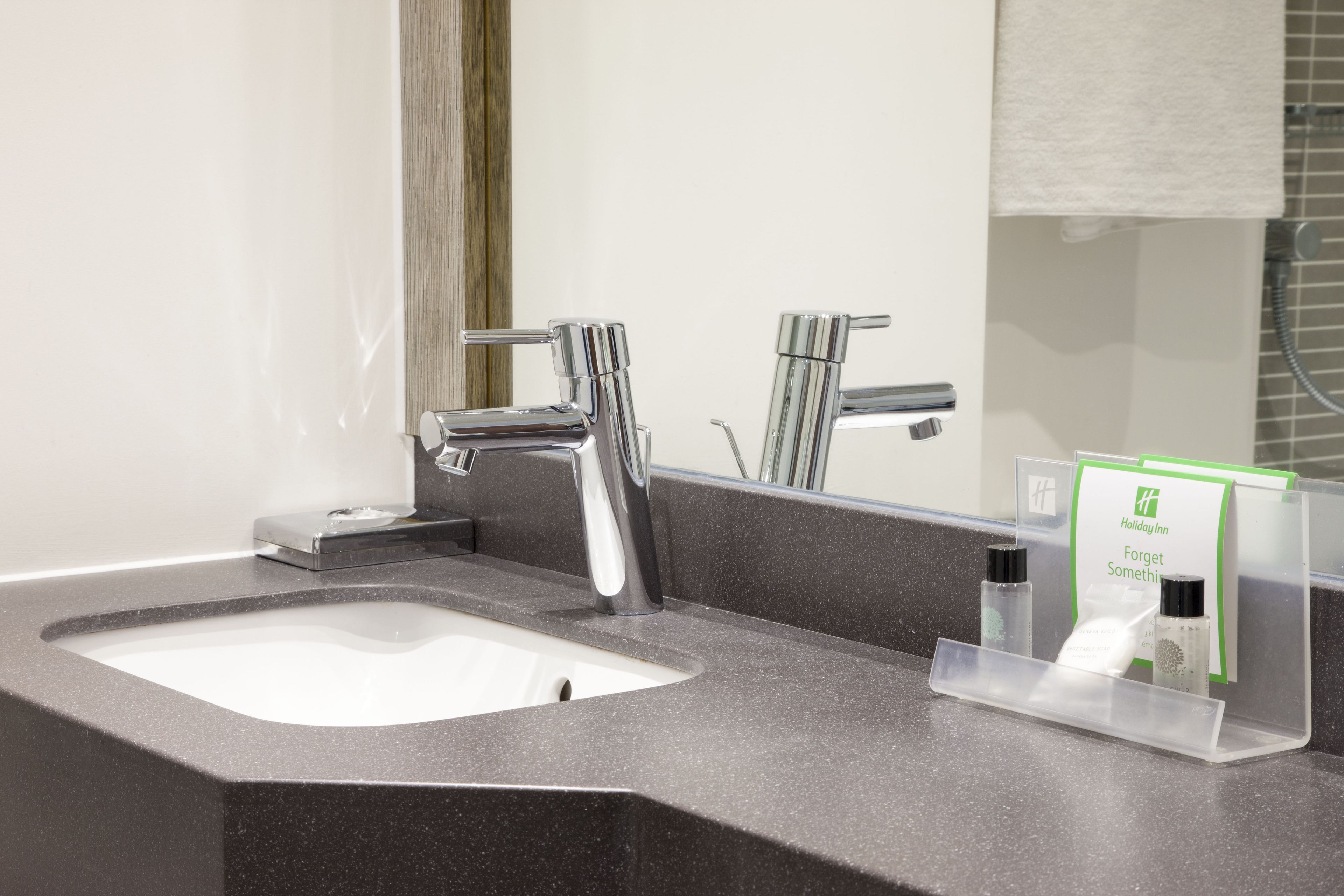 Un baño moderno con un lavabo grande, grifos cromados y un espejo. Hay un perchero y un dispensador de jabón en la encimera.