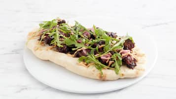 A flatbread with toppings on a white plate.