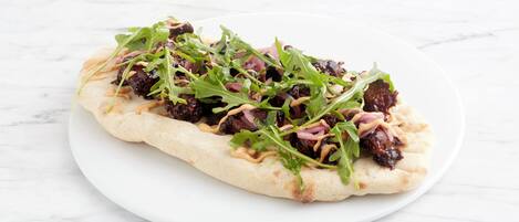 A flatbread with toppings on a white plate.