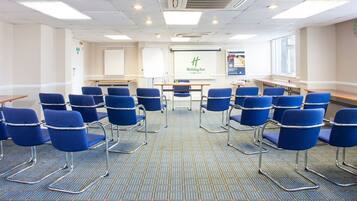 A conference room with blue chairs arranged in rows, a presentation screen, and a Holiday Inn logo.