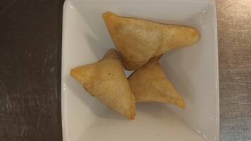 Un plato cuadrado y blanco con tres pastas triangulares sobre una superficie oscura.