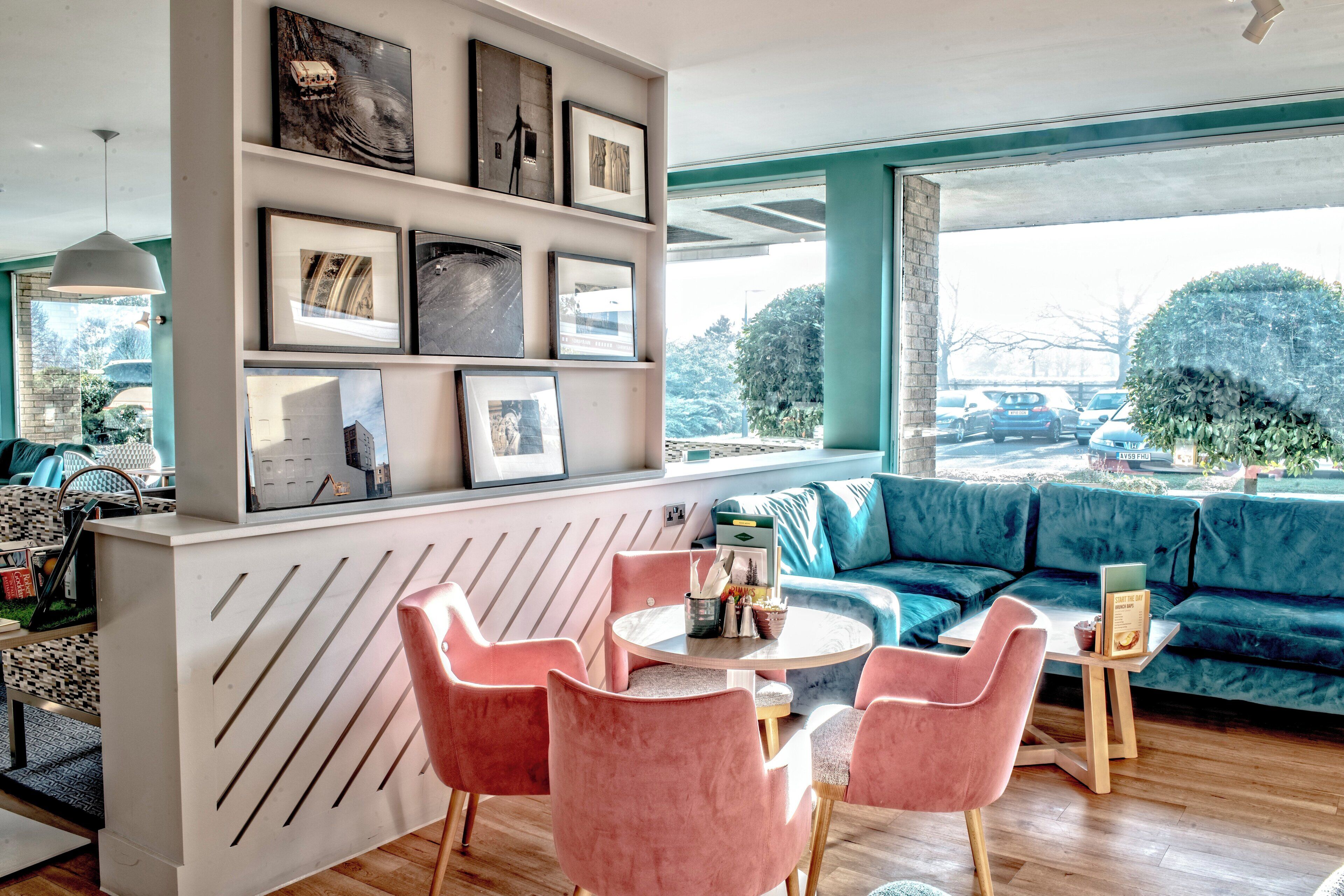 A modern living room with a blue sofa, pink chairs, a coffee table, and a wall with framed pictures.
