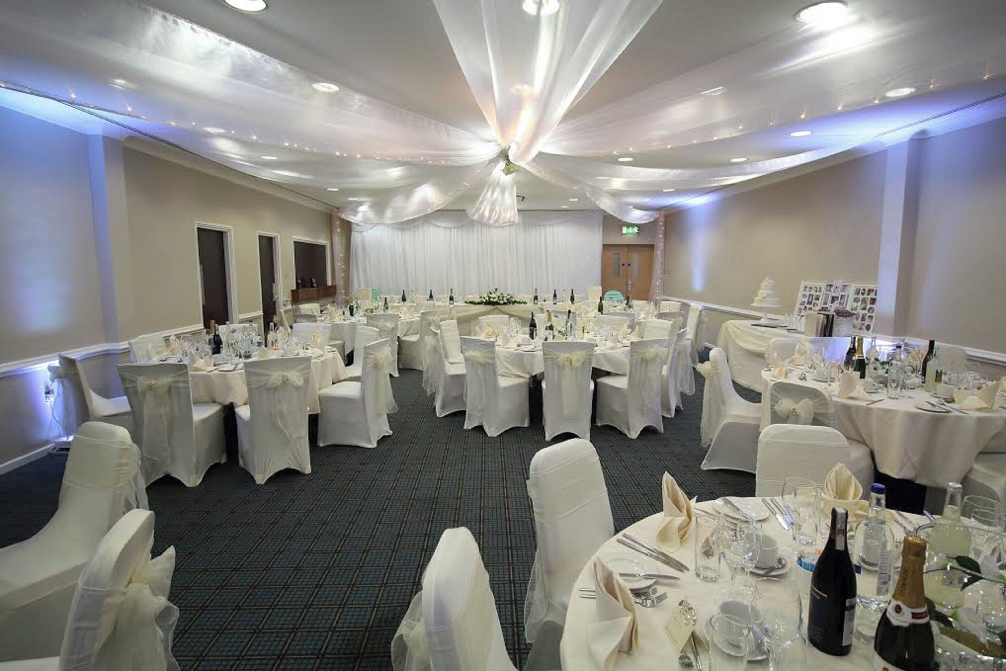 Un salón de banquetes con mesas redondas dispuestas para comer, cortinas blancas y una araña de cristal.
