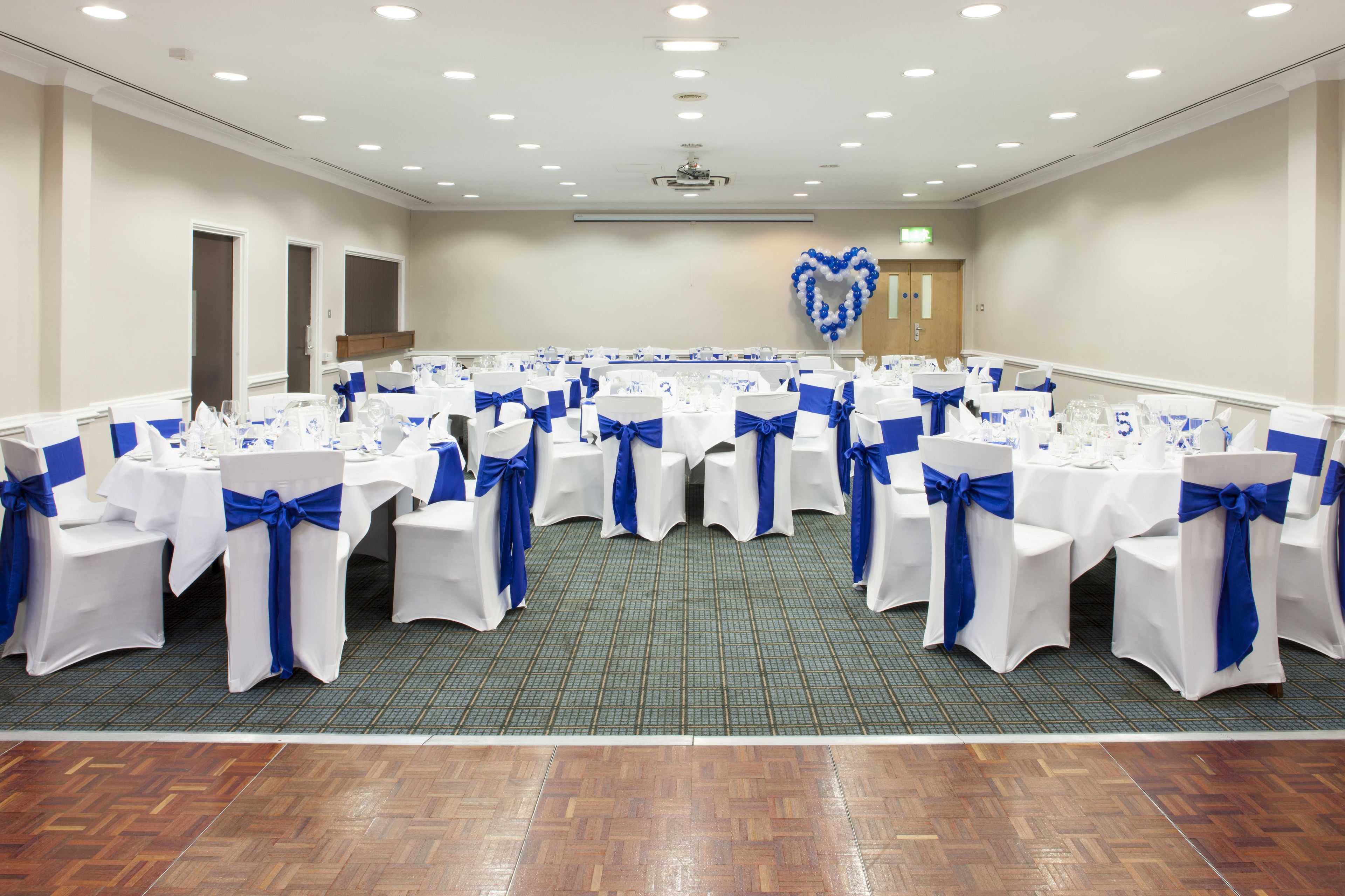 Un salón de conferencias amplio con filas de mesas y sillas, cada una con manteles blancos y cintas azules.