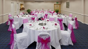 A banquet hall with round tables, white tablecloths, and chairs with pink sashes.