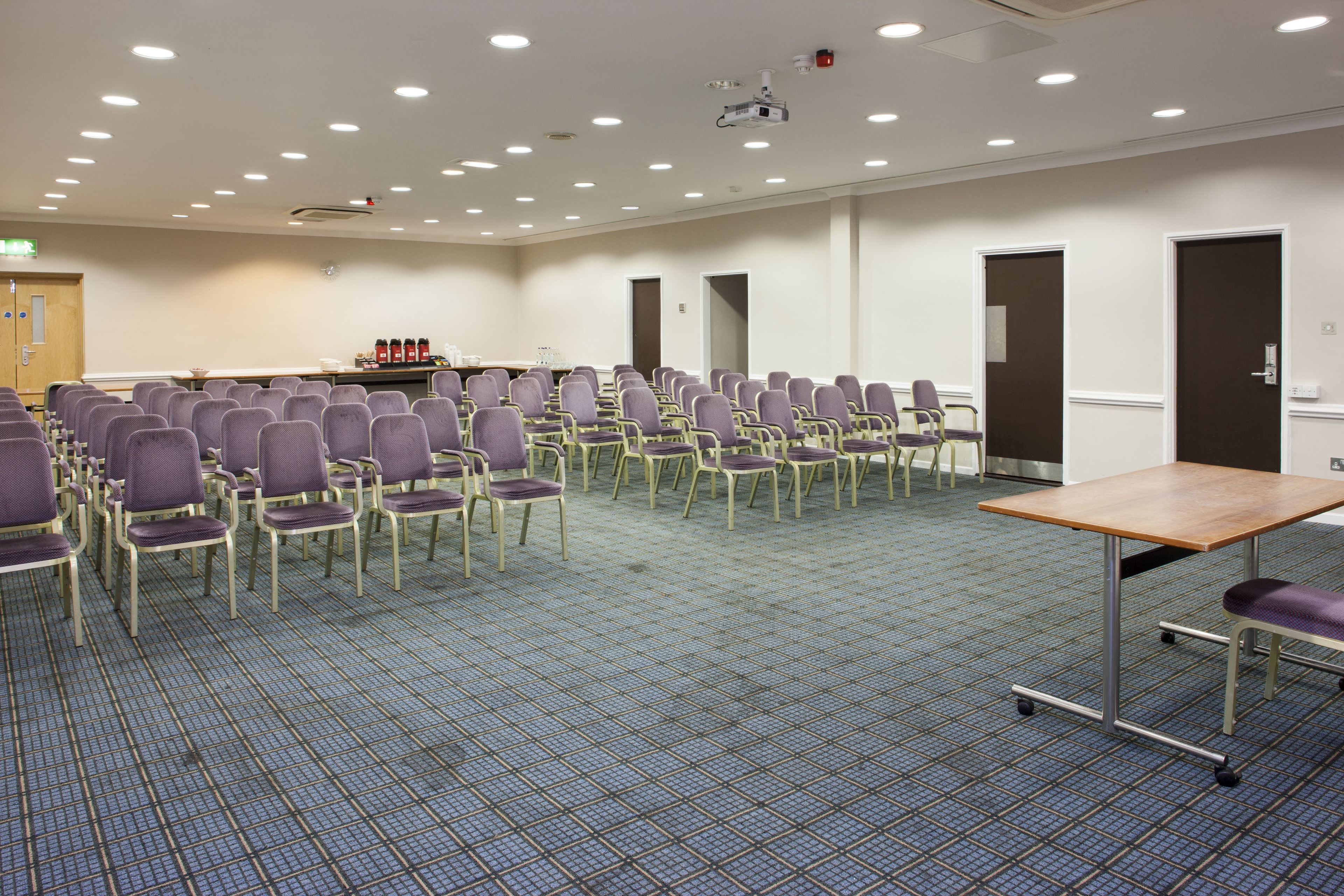 Un salón de conferencias con filas de sillas, un proyector y una mesa.