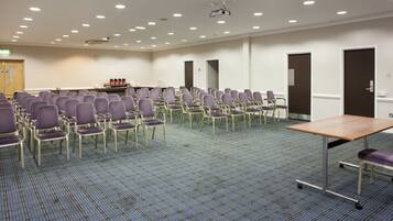 Un salón de conferencias con filas de sillas, un proyector y una mesa.