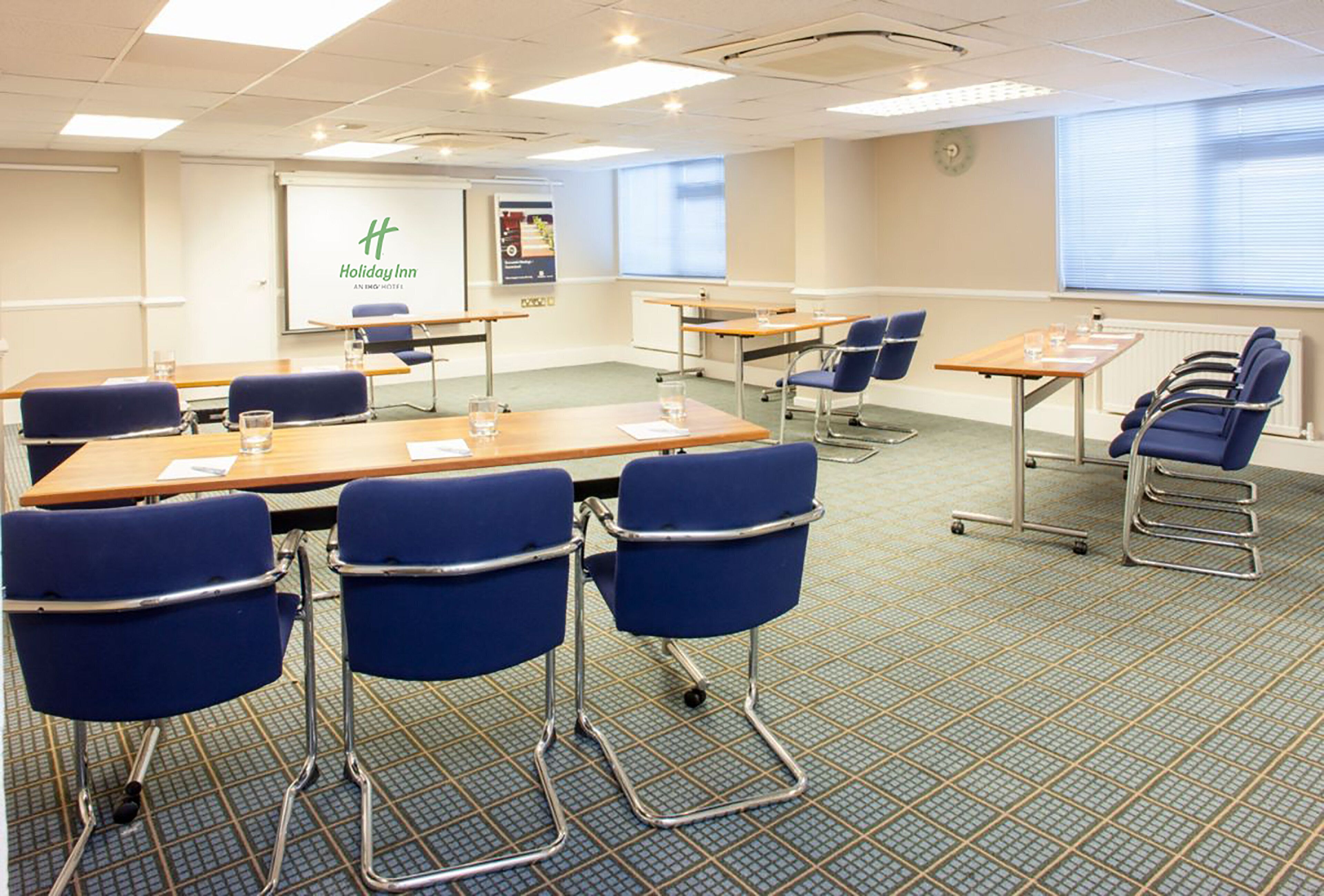 A conference room with tables, chairs, and a presentation screen.