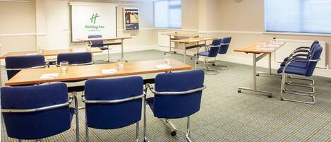 A conference room with tables, chairs, and a presentation screen.