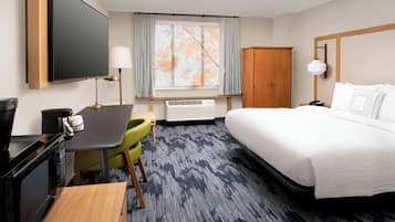 A hotel room with a bed, a desk with a computer, a chair, a TV, a wardrobe, and a window with curtains.