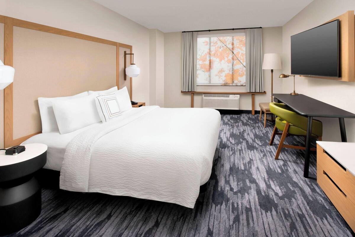 Ein Hotelzimmer mit einem Bett, einem Schreibtisch, einem Sessel, einem Fernseher und einem Fenster mit Vorhängen.