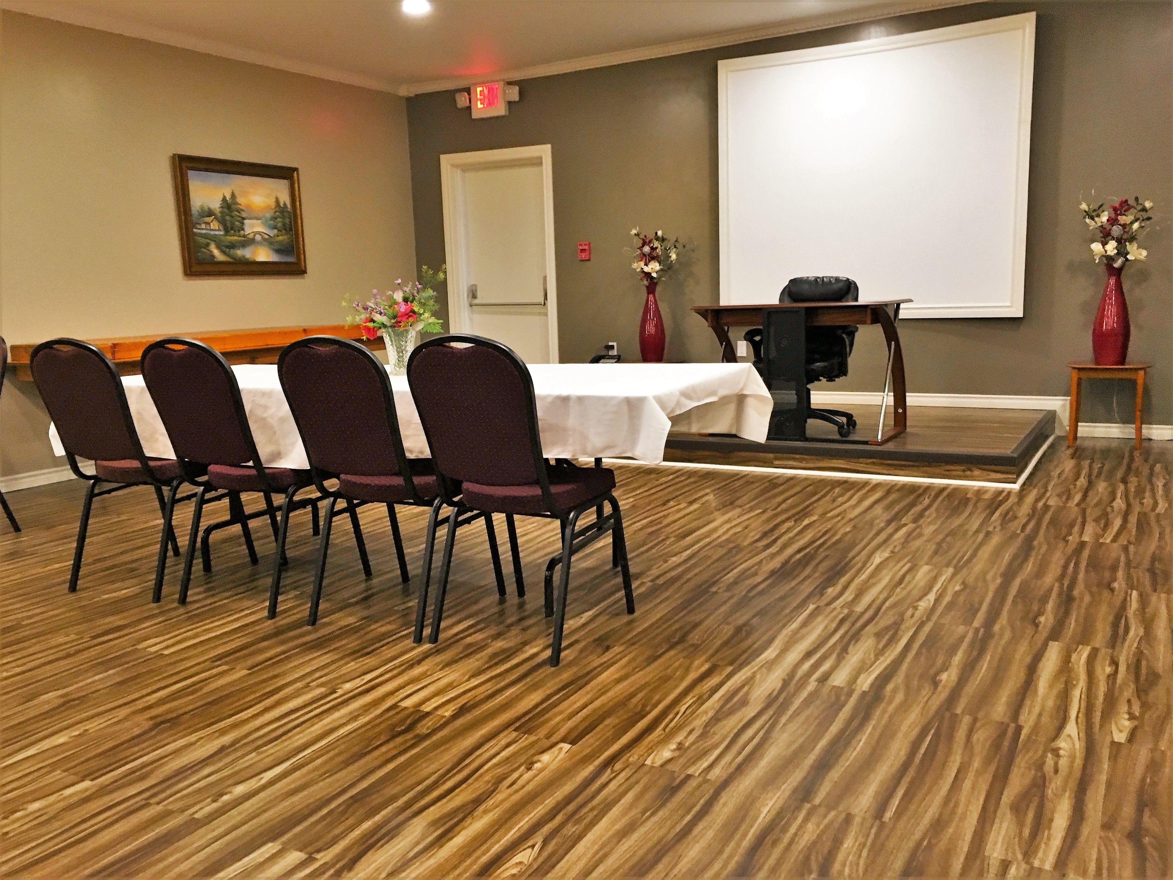 A conference room with a white table, four chairs, a projector screen, and two vases with flowers.