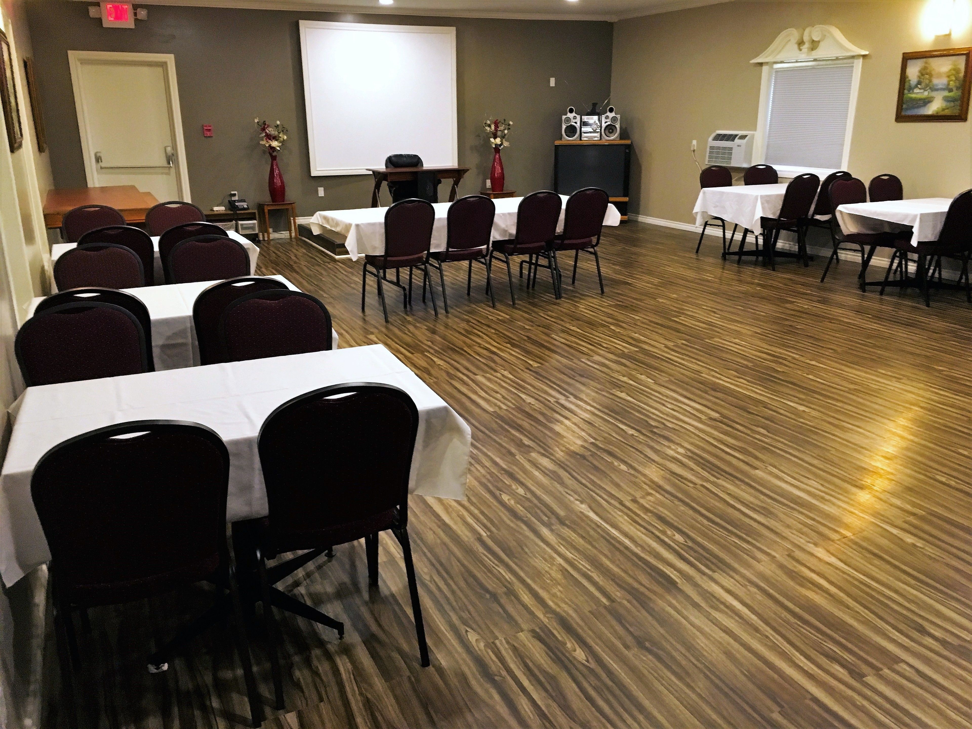 A conference room with multiple tables and chairs, a projector screen, and an air conditioning unit.