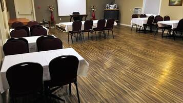 A conference room with multiple tables and chairs, a projector screen, and an air conditioning unit.