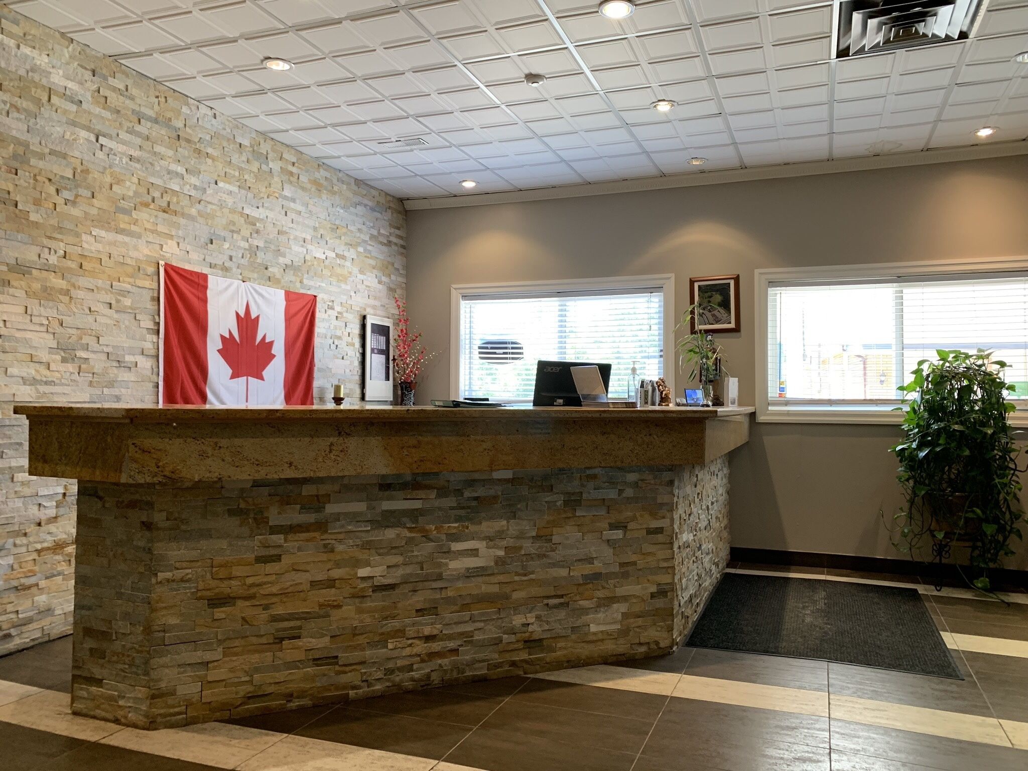 A reception area with a stone counter, a Canadian flag, a computer, and a window with blinds.