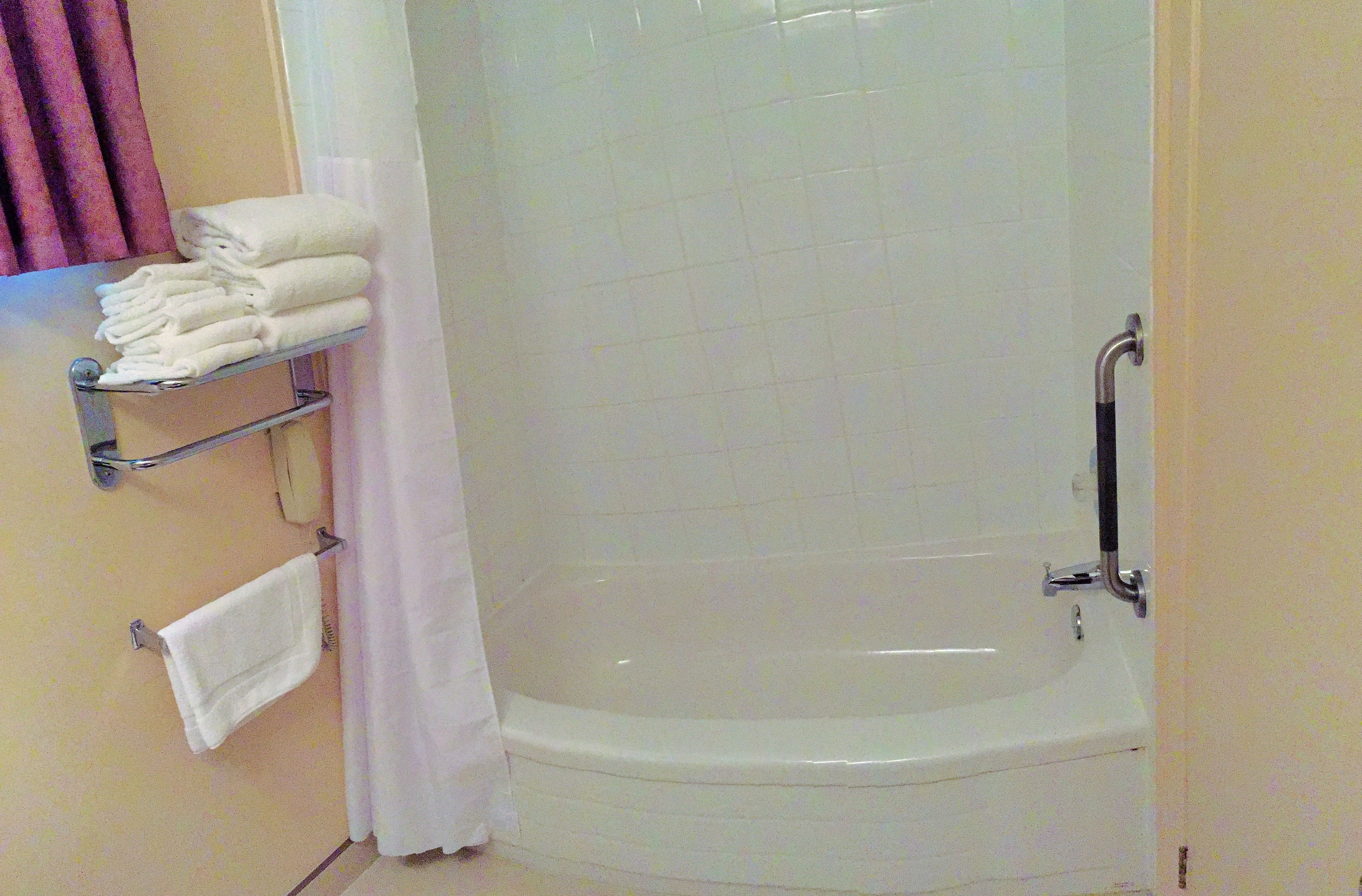Un baño con bañera, un perchero con toallas dobladas y cortina de ducha.