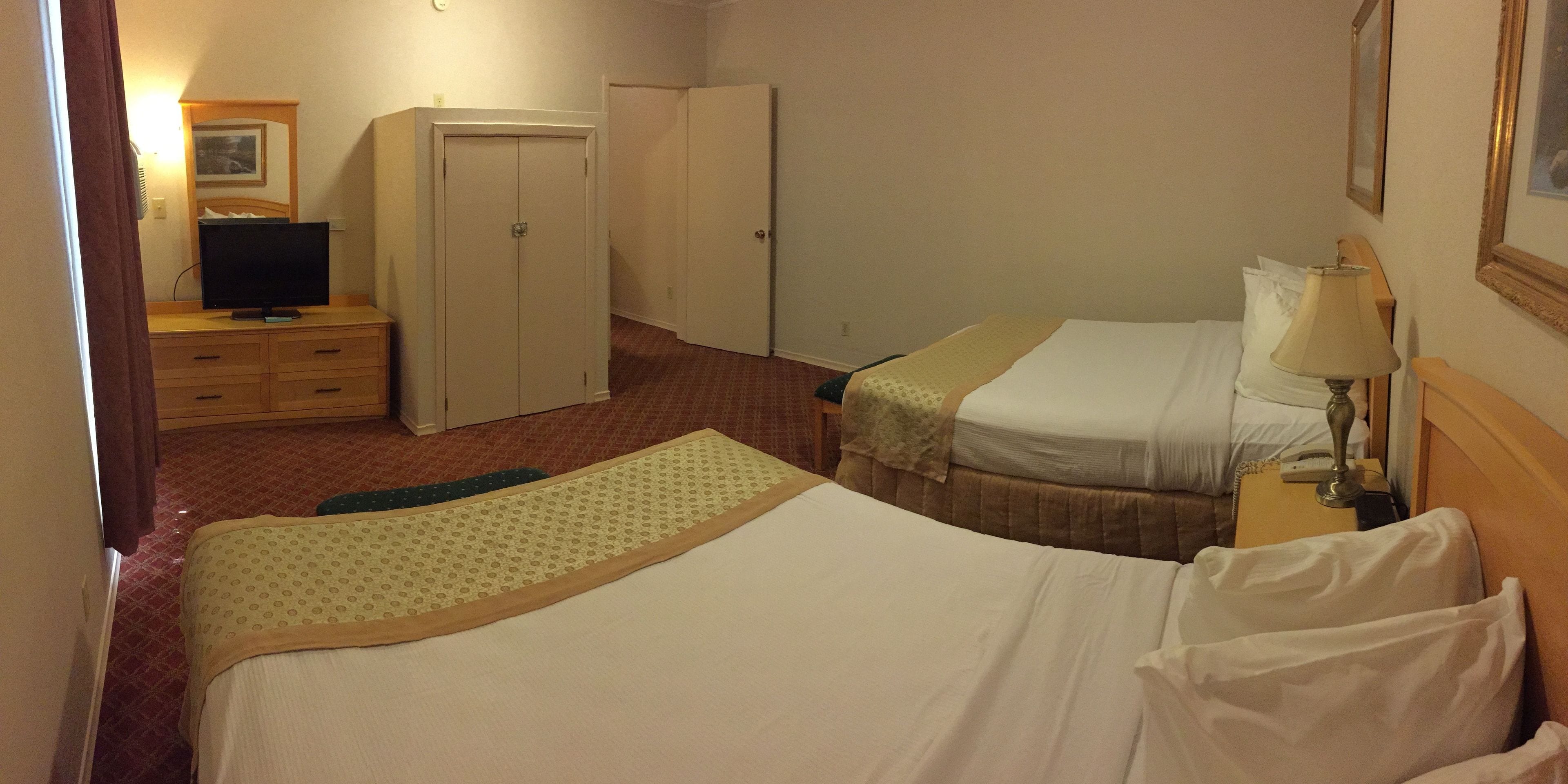 A hotel room with two beds, a desk with a lamp, a television, and a wardrobe.