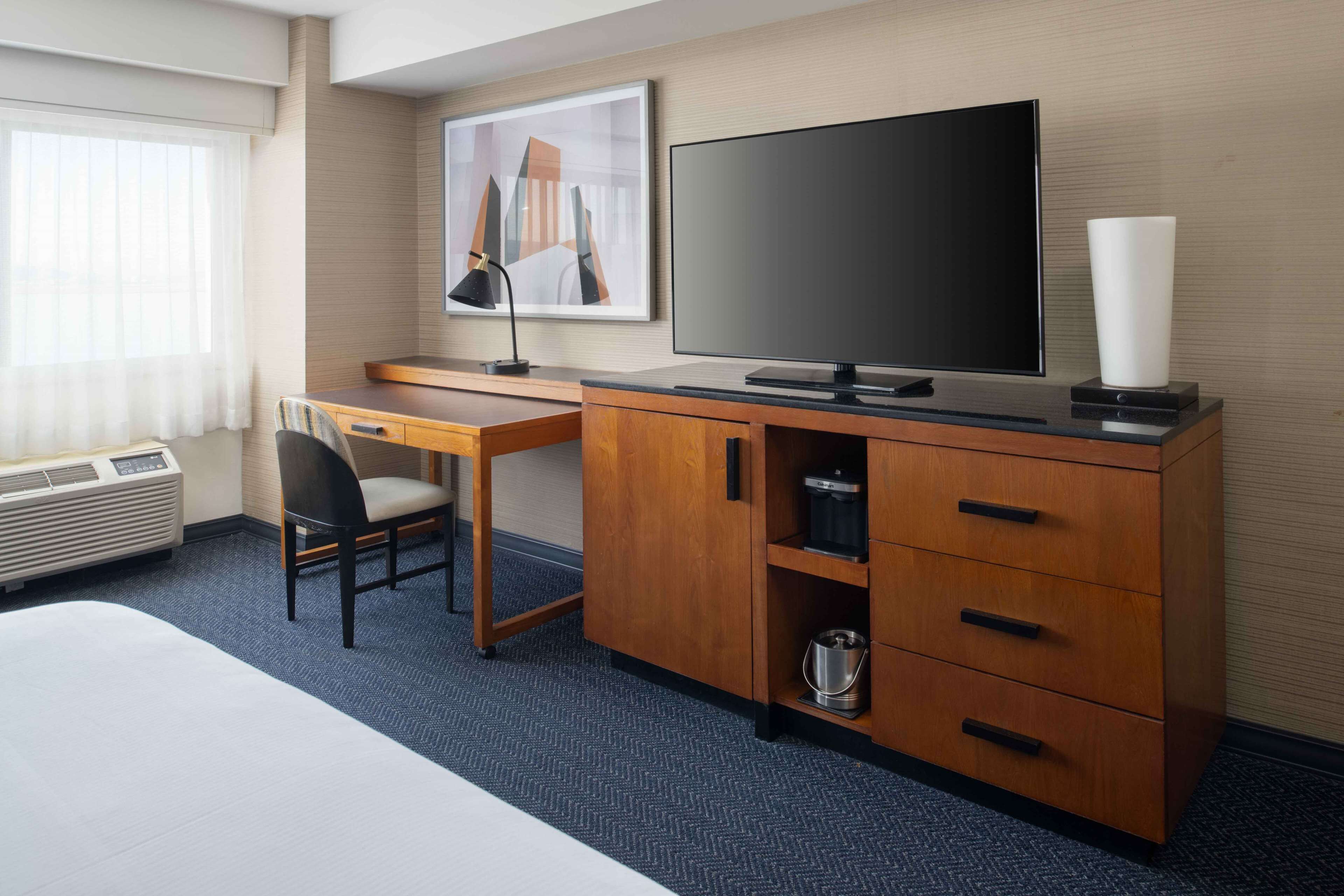 Habitación de hotel con una cama, un escritorio con silla, televisión, armario y un cuadro en la pared.