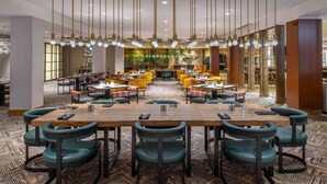 A spacious dining area with multiple tables and chairs, featuring a patterned carpet and pendant lighting.