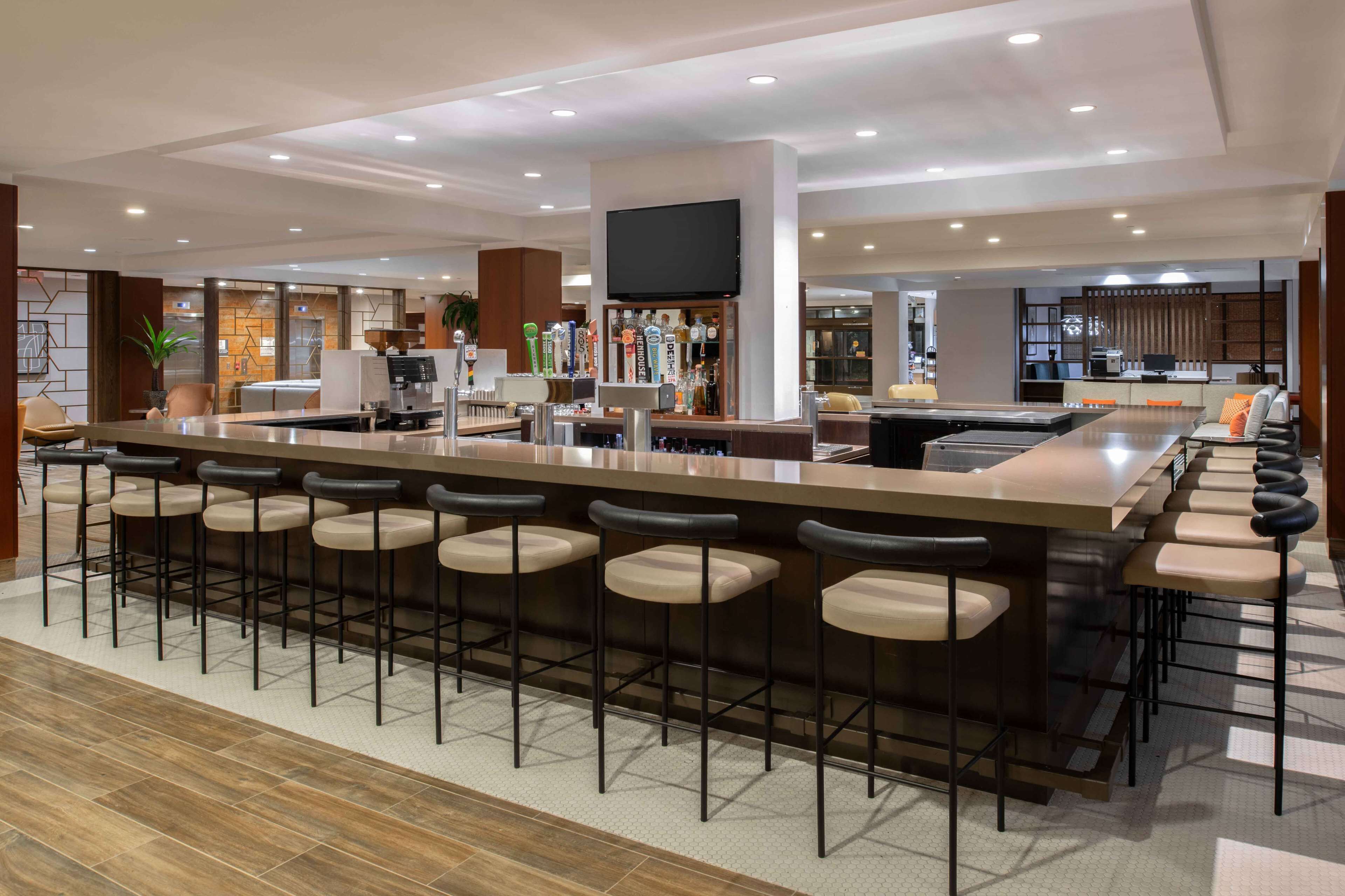 A modern bar area with a long counter, multiple stools, and a television mounted above.