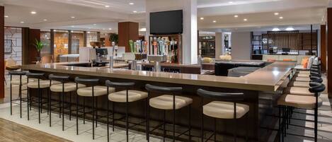 A modern bar area with a long counter, multiple stools, and a television mounted above.