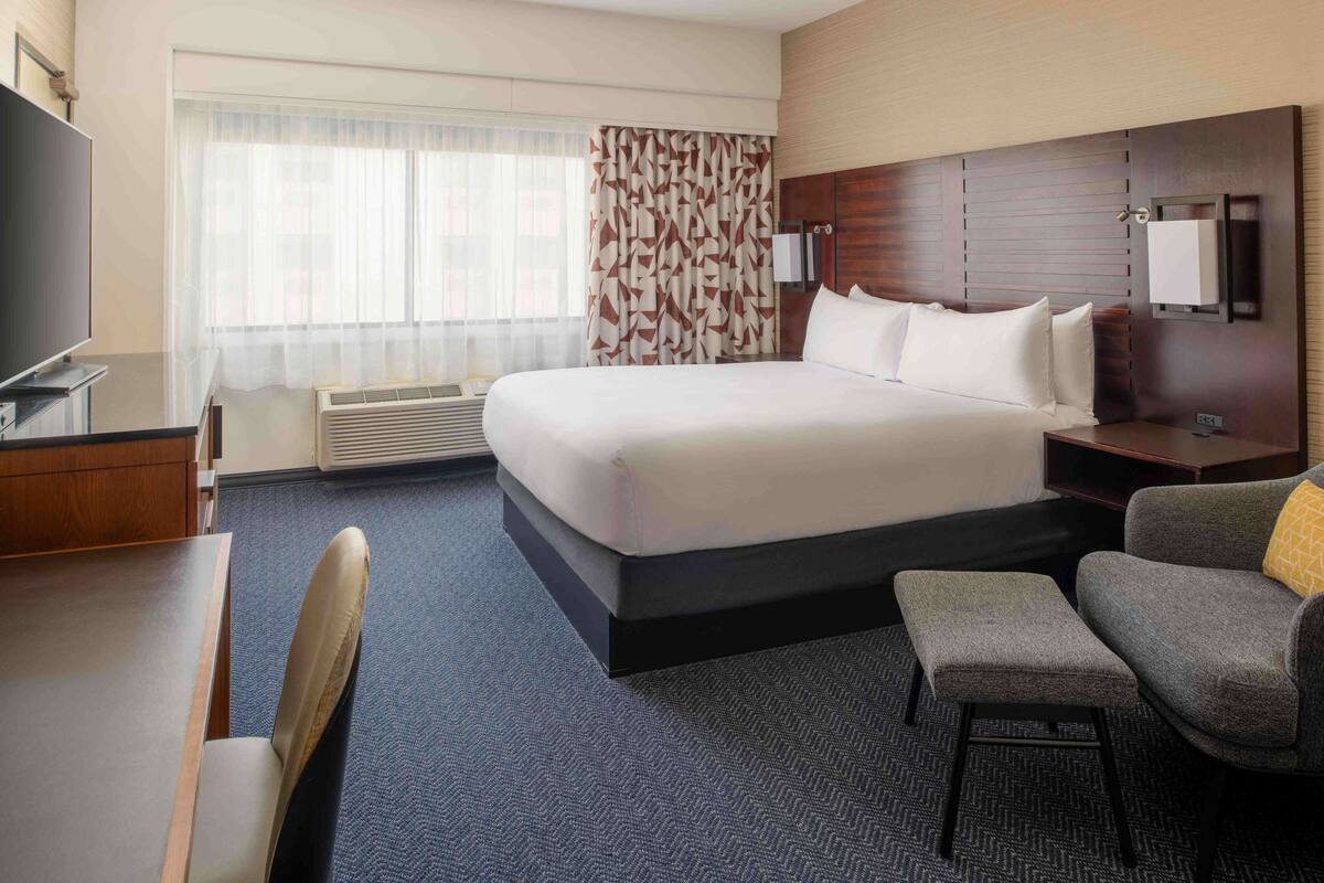 A hotel room with a large bed, a desk, a chair, and a TV.