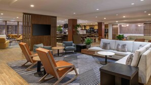 A modern hotel lobby with a seating area, a bar, and a television screen.