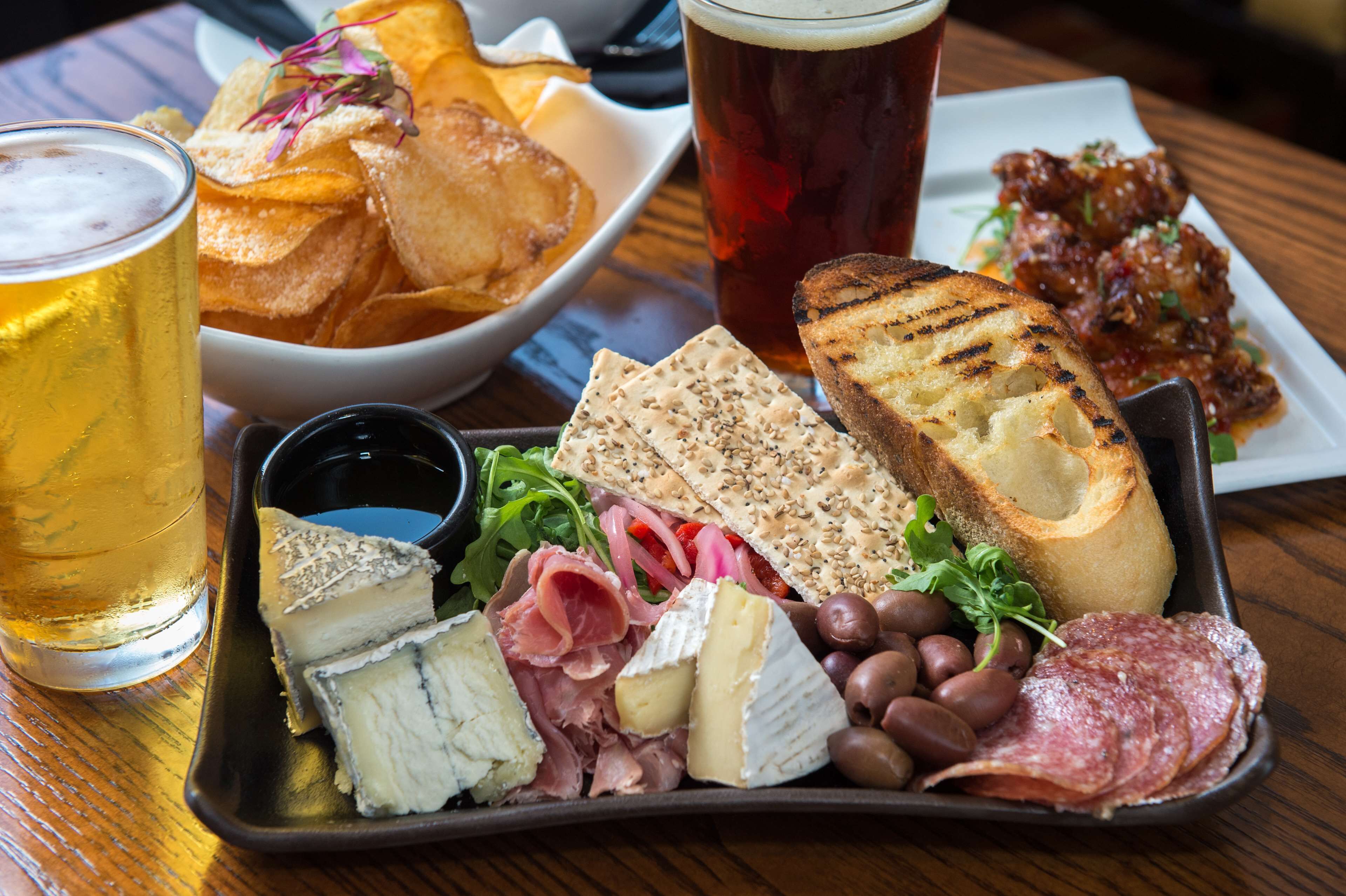 A charcuterie board with cheese, meats, olives, and bread, accompanied by a beer and chips.