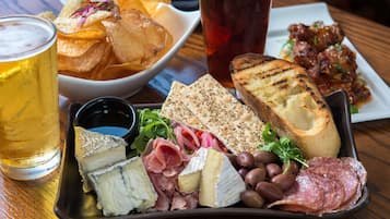 A charcuterie board with cheese, meats, olives, and bread, accompanied by a beer and chips.