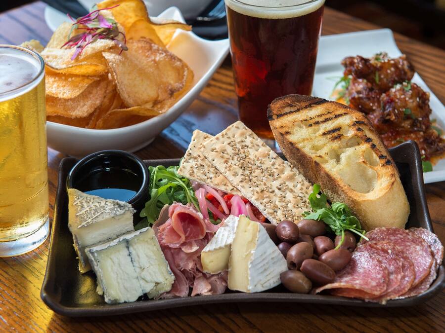Een charcuterieplank met kaas, vleeswaren, olijven en brood, vergezeld van een biertje en chips.