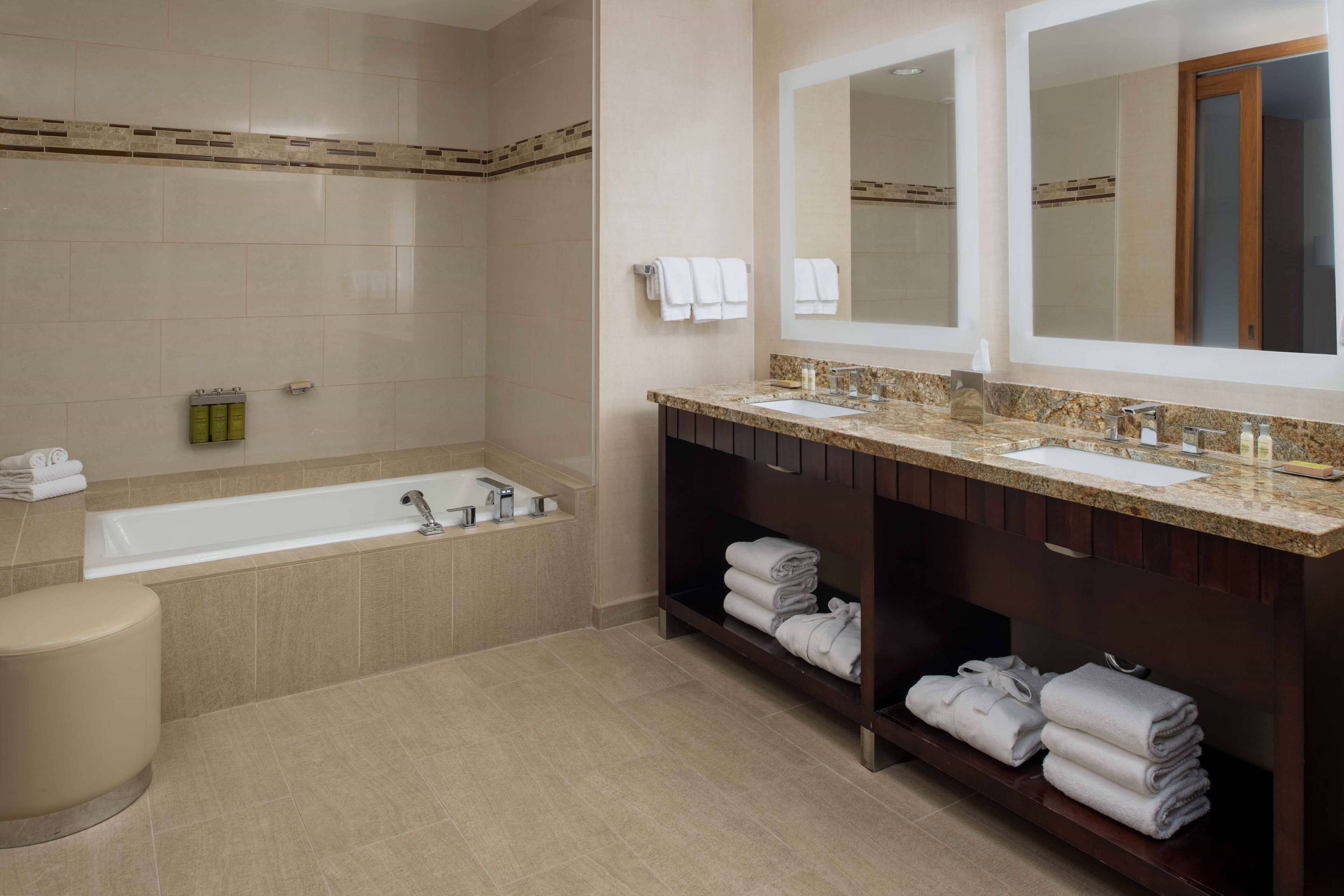 Un baño moderno con bañera, dos lavamanos y un espejo grande.