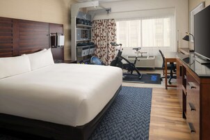 Una habitación de hotel con una cama grande, un escritorio con una computadora, un televisor y una bicicleta estática.