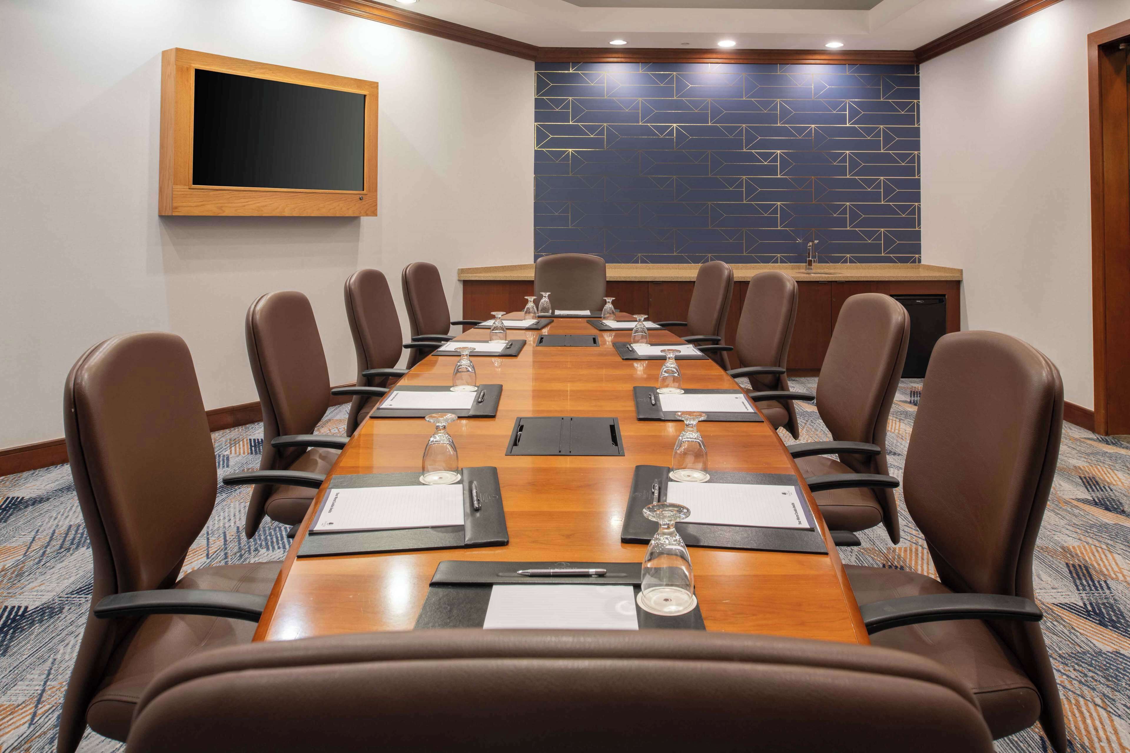 A conference room with a long table, brown leather chairs, a large screen, and a patterned wall.