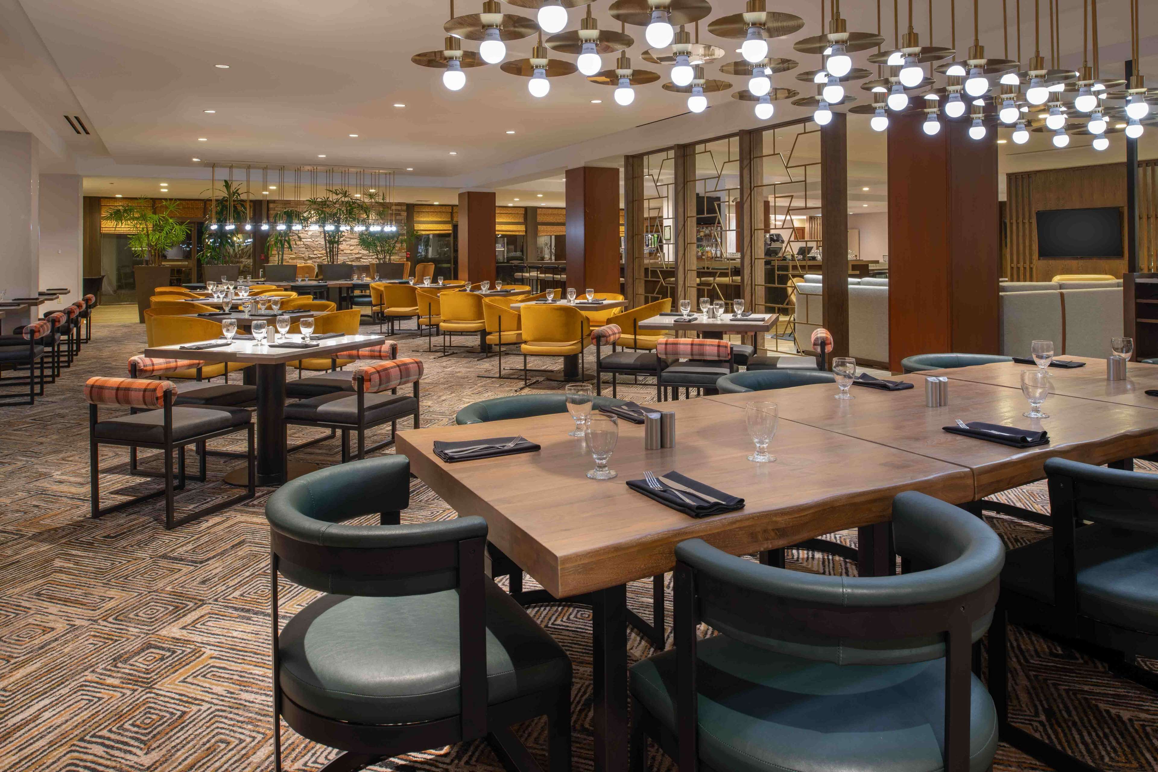 A spacious dining area with multiple tables and chairs, modern pendant lighting, and a patterned carpet.