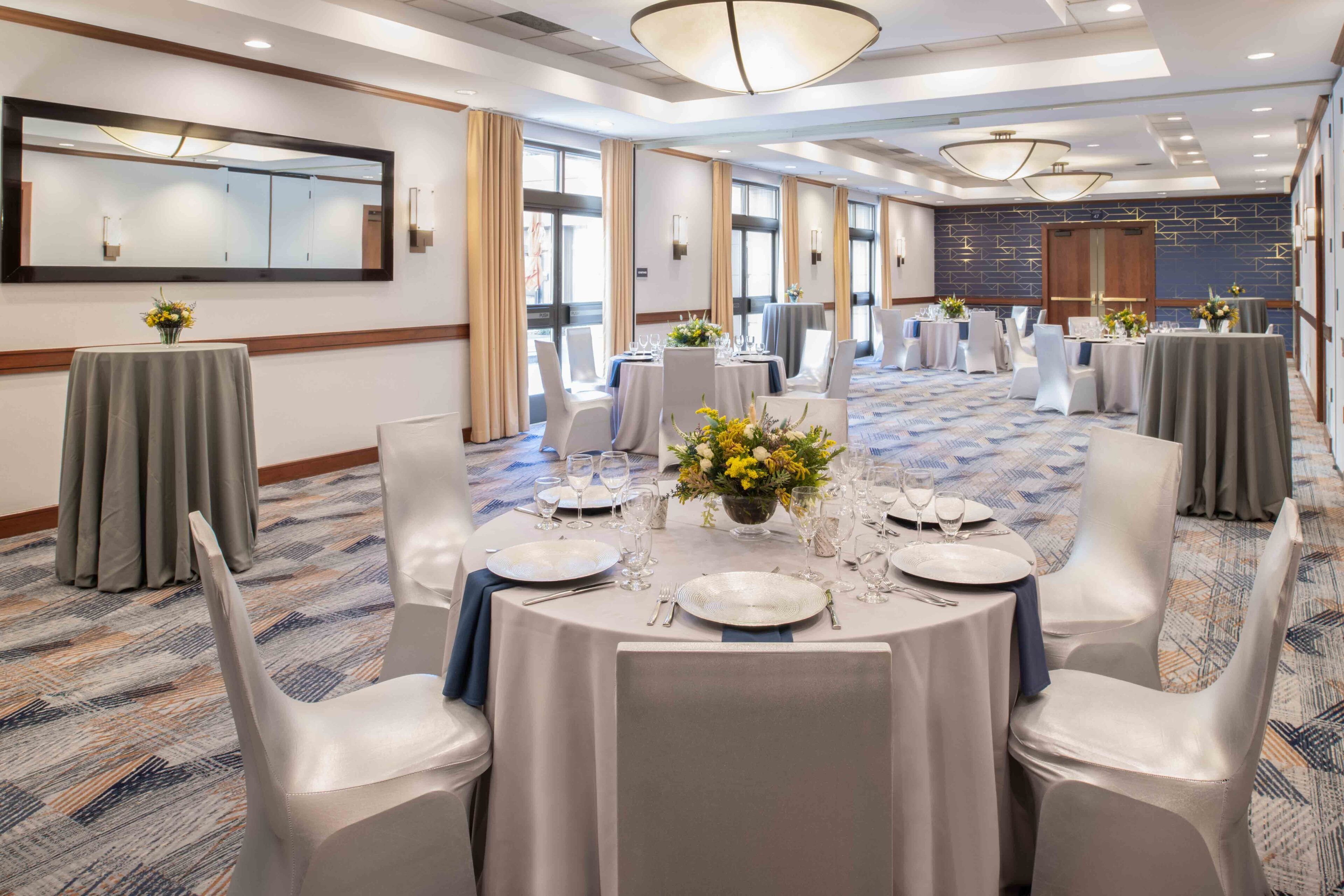 A banquet hall with round tables set for dining, white chairs, and a large mirror on the wall.