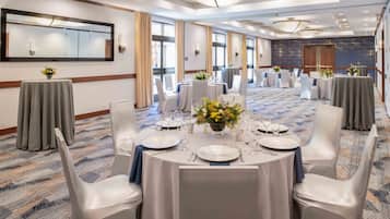 A banquet hall with round tables set for dining, white chairs, and a large mirror on the wall.